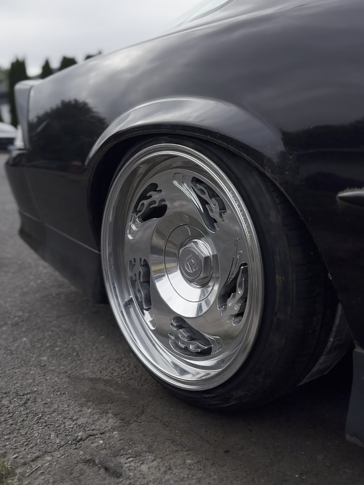 Close-up of a black car with a shiny chrome wheel with flame pattern on a road.