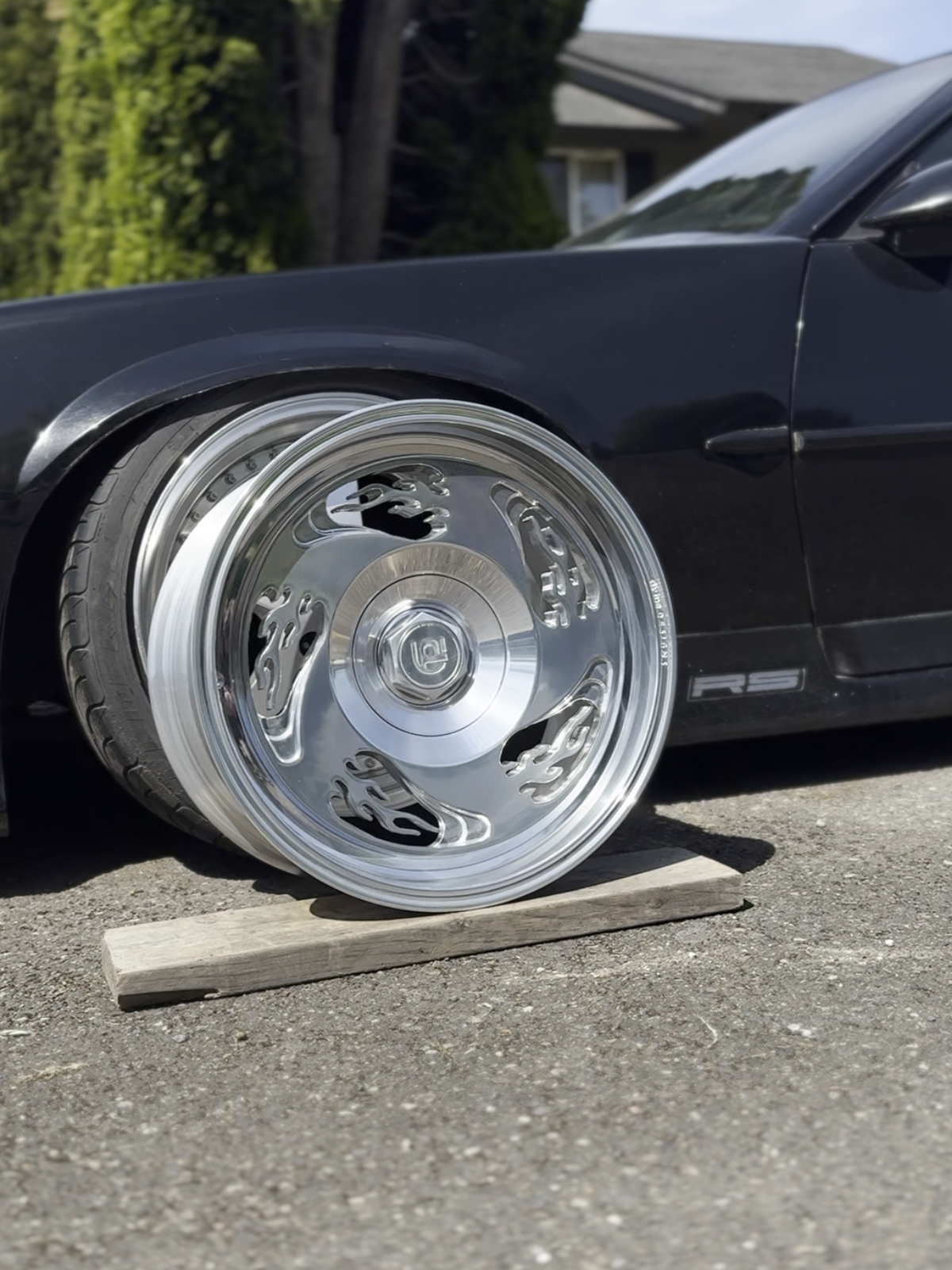 Close-up of a car wheel with a shiny flame pattern wheel on a wooden block outdoors.