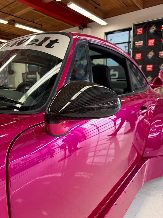 Close-up image of a one-piece seamless carbon fiber aero mirror for Porsche vehicles, displayed on a red car.