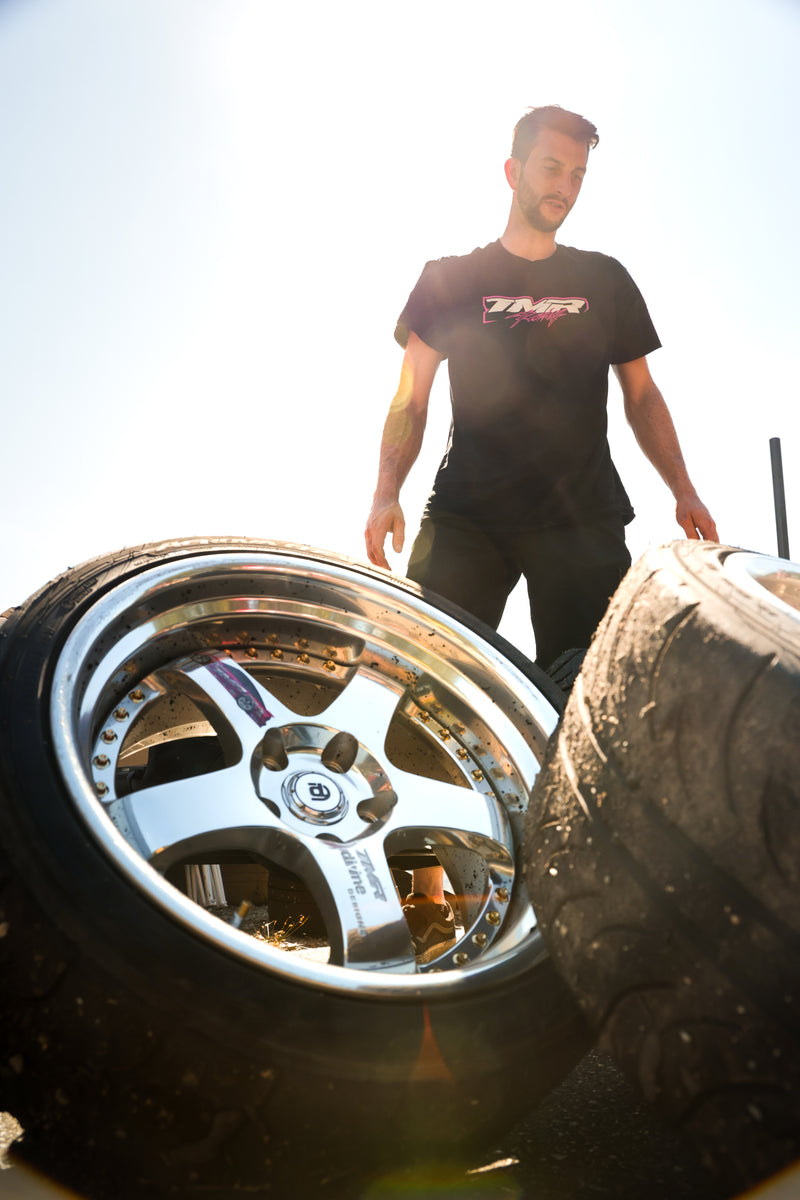 Man standing next to a shiny car wheel with a blurred background
