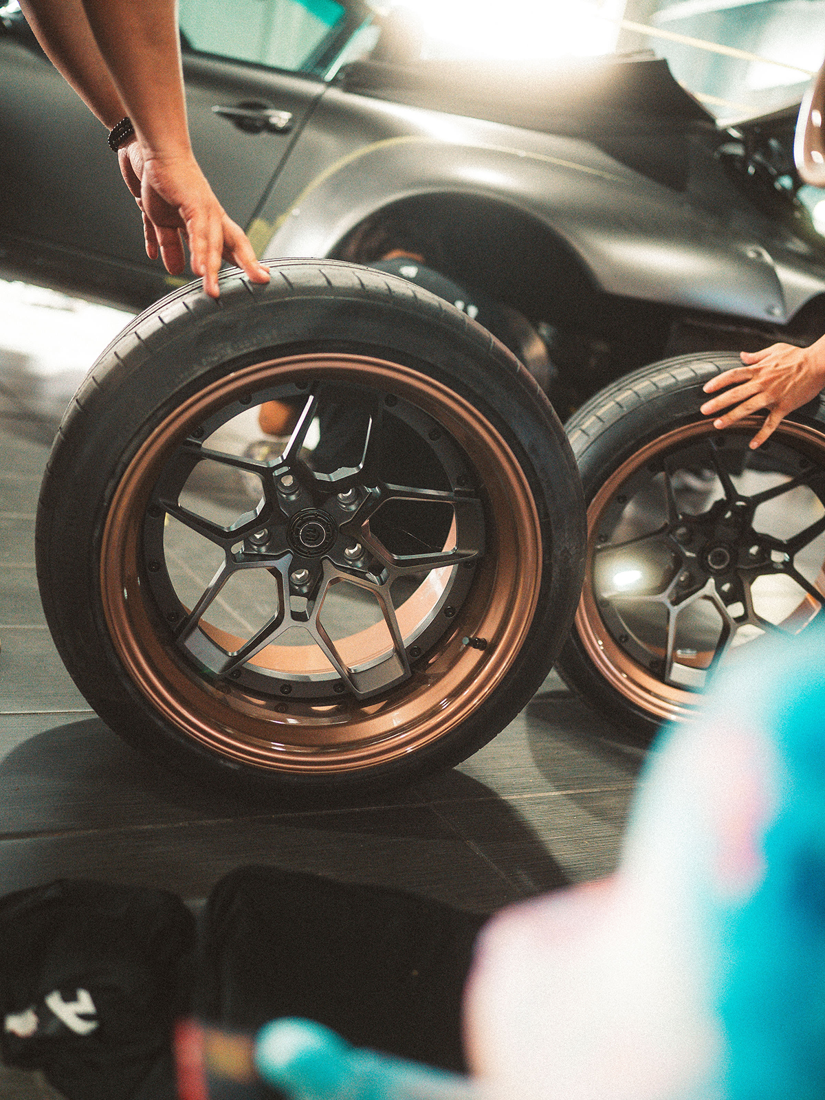 Two car wheels with bronze rims being held by a person in a car showroom.