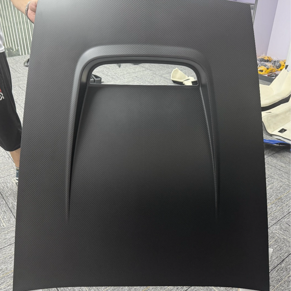 Black car hood panel held by a person on a concrete floor.
