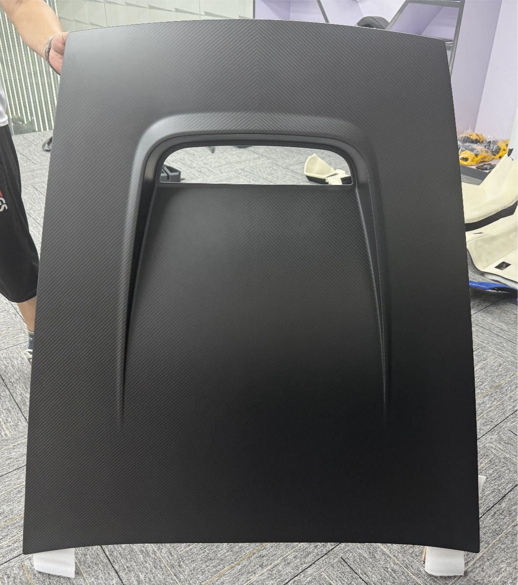 Black car hood panel held by a person on a concrete floor.