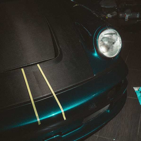Close-up of a blue Porsche with carbon fiber hood on a dark background