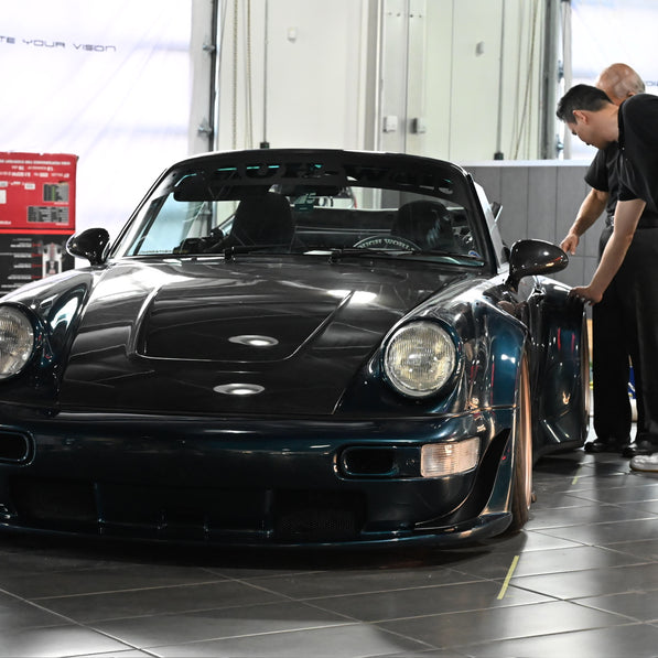Two men inspecting a blue sports car in a garage.