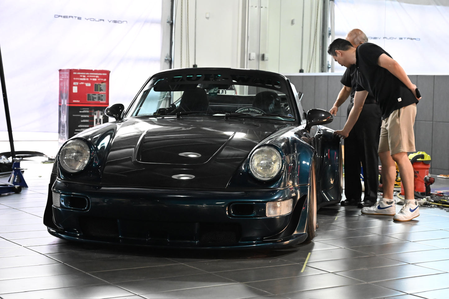 Two men inspecting a blue sports car in a garage.