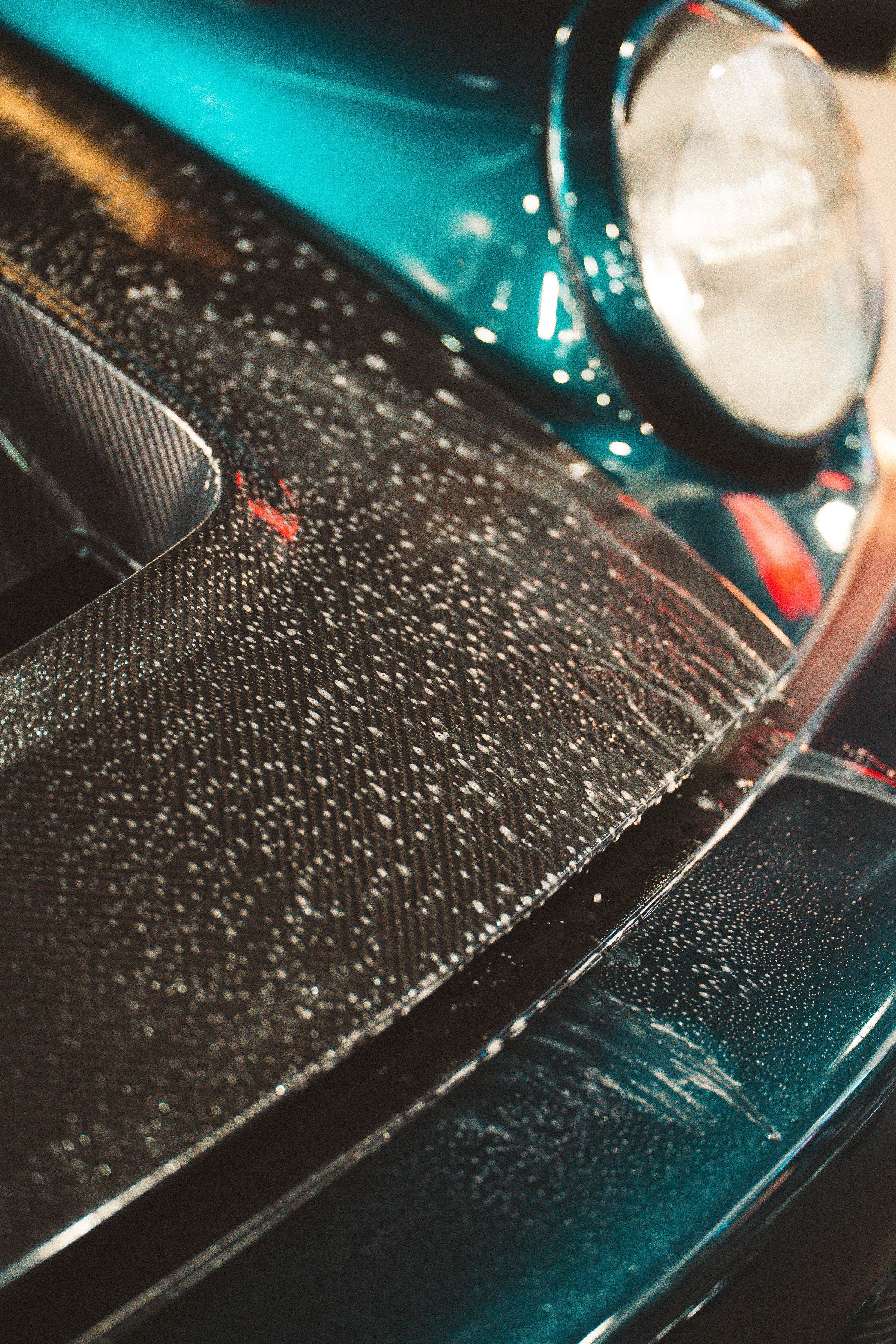 Close-up of a car's headlight and front bumper with water droplets on a wet surface.