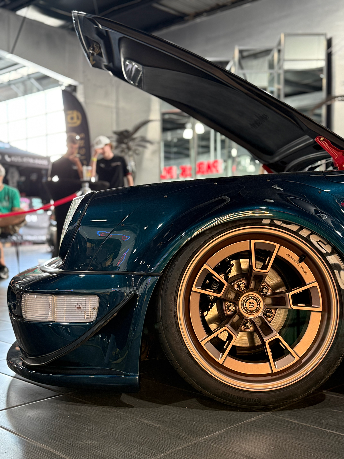 Close-up of a teal car with gold rims in an indoor setting