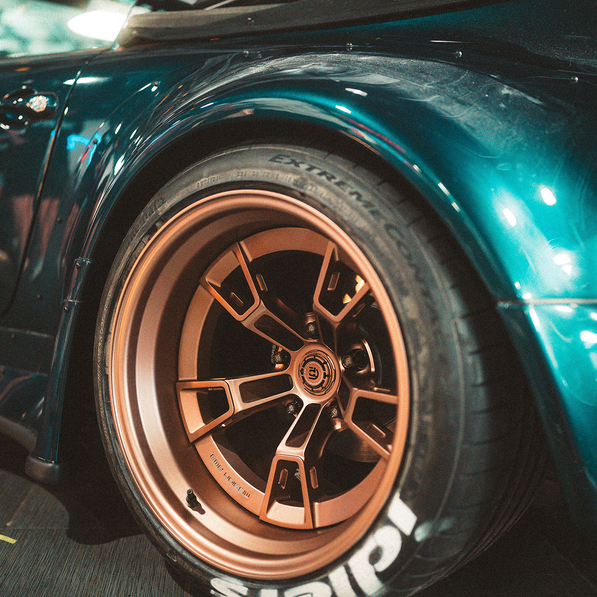 Close-up of a car wheel with a bronze rim branding on a teal vehicle.
