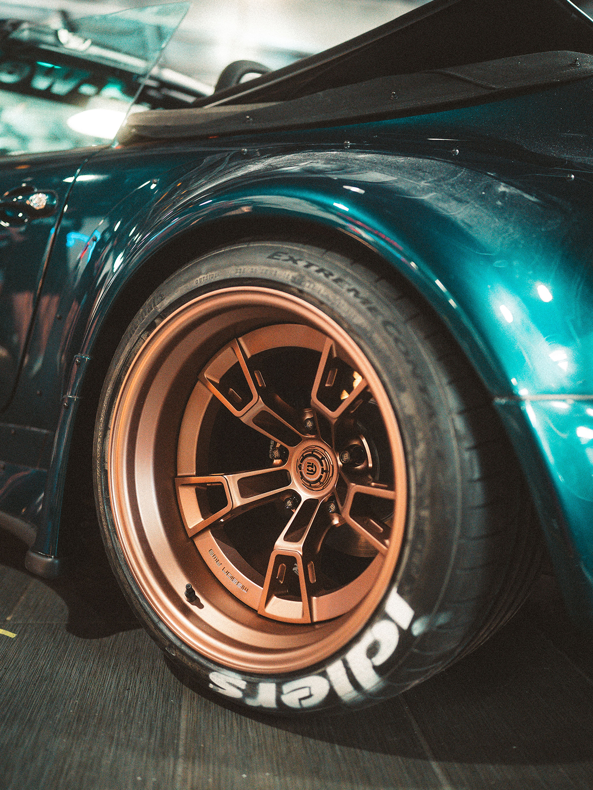 Close-up of a car wheel with a bronze rim branding on a teal vehicle.