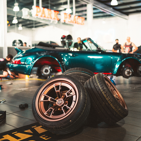Three car wheels on a floor with a teal sports car in the background.