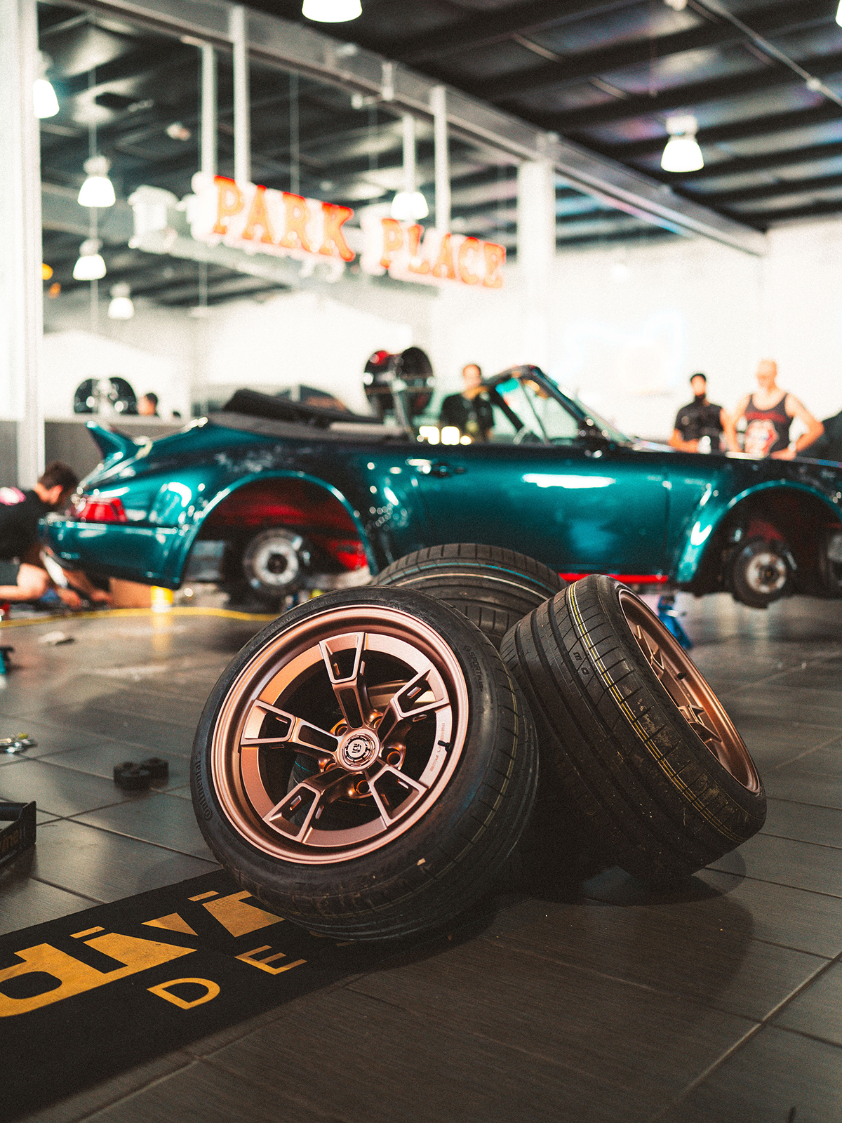 Three car wheels on a floor with a teal sports car in the background.
