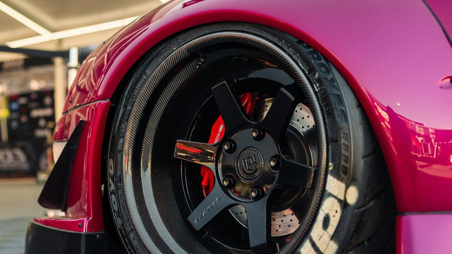 Close-up of a red car wheel with a black rim and tire on a checkered floor.