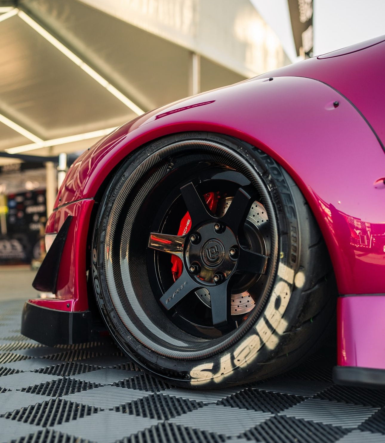 Close-up of a red car wheel with a black rim and tire on a checkered floor.