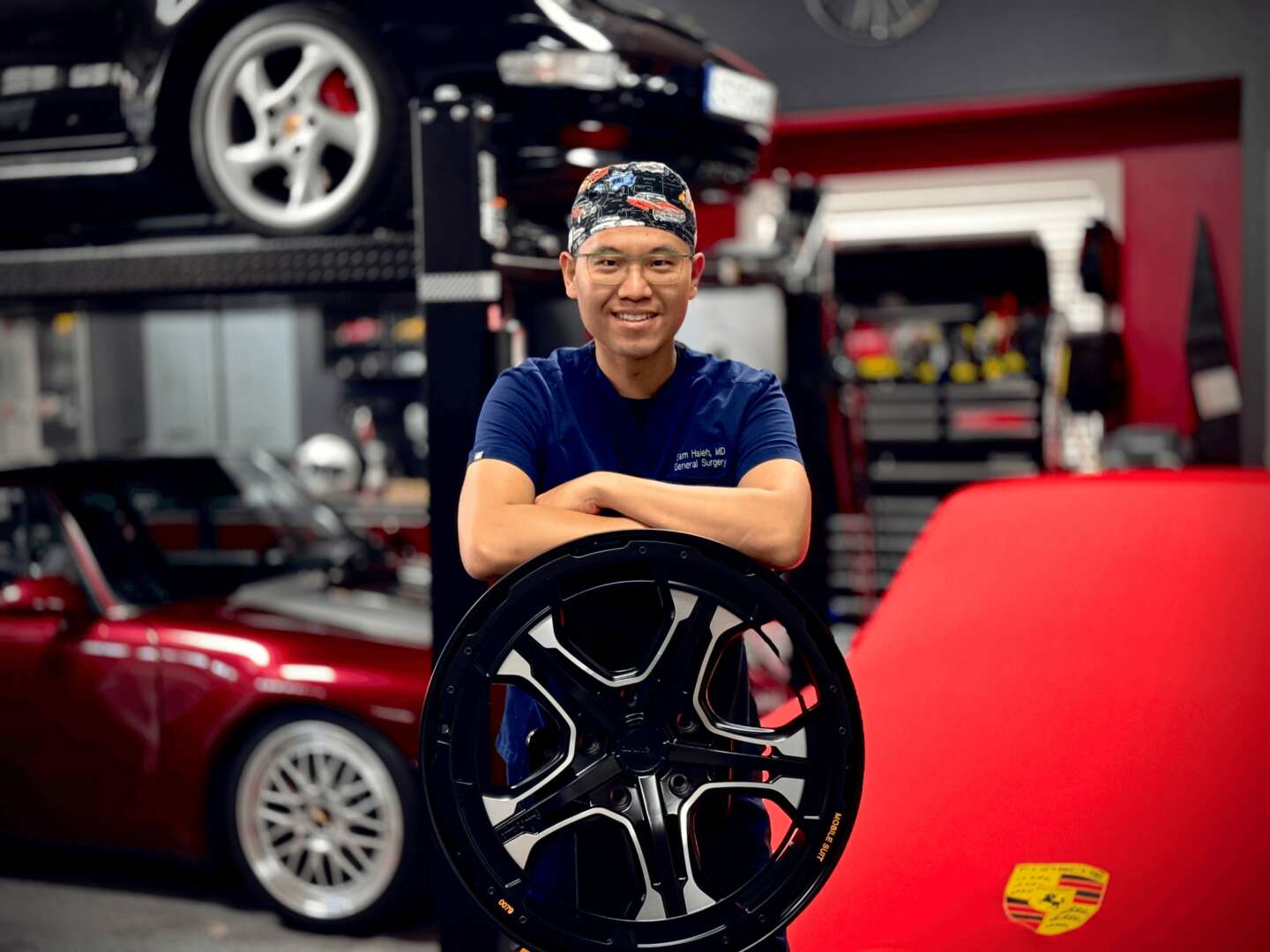 Person holding a car wheel in a garage with red cars and tools in the background