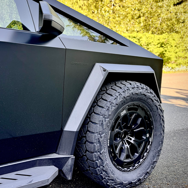 Close-up of a modern vehicle's wheel and fender on a road with trees in the background