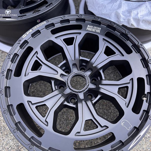 Close-up of a black alloy wheel with visible branding on a concrete surface.