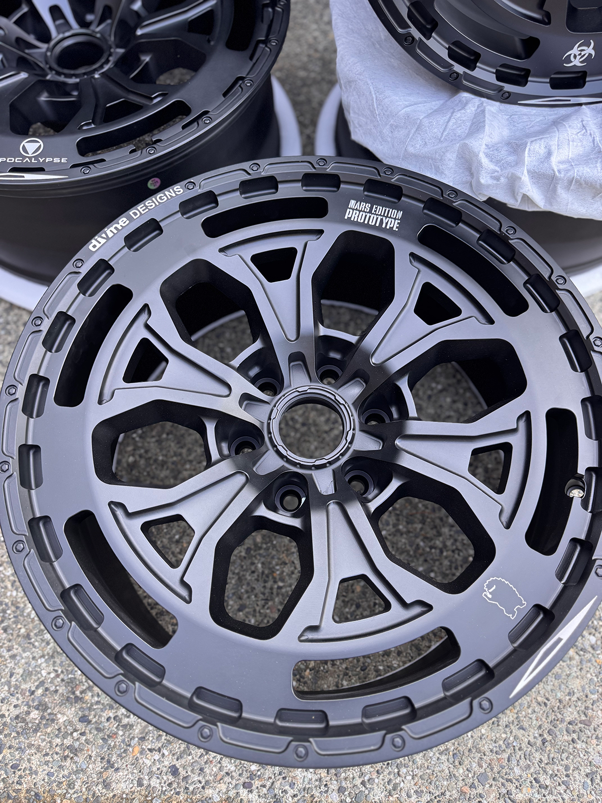 Close-up of a black alloy wheel with visible branding on a concrete surface.