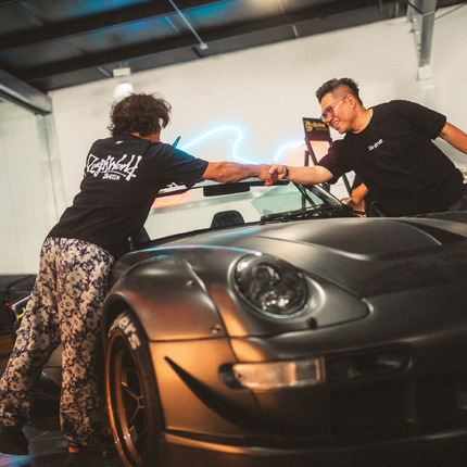 Two people shaking hands in front of a car in a garage setting