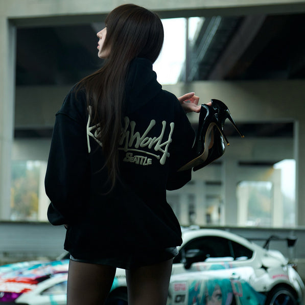Person wearing a black hoodie with white text, standing in front of a colorful car.