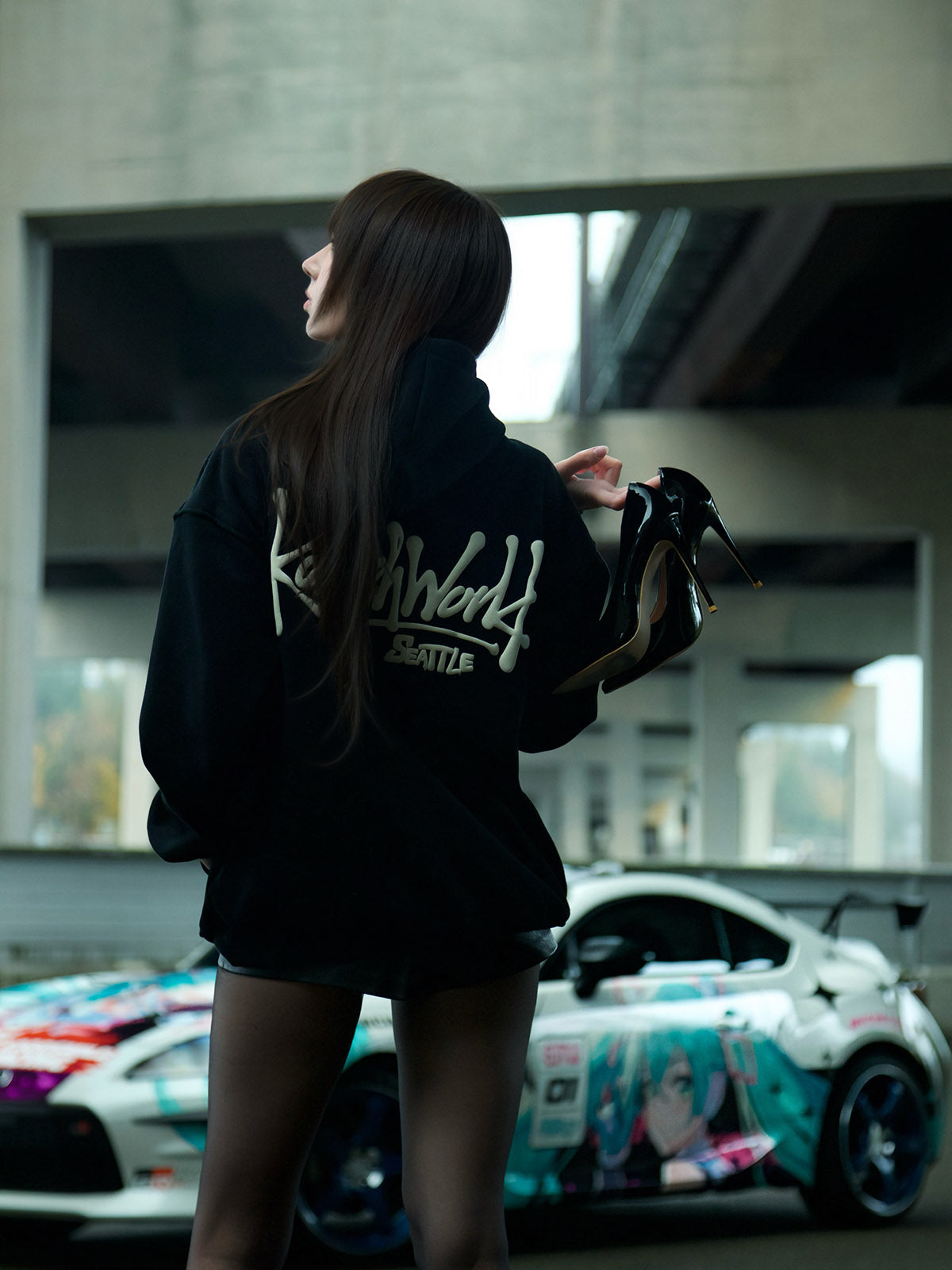 Person wearing a black hoodie with white text, standing in front of a colorful car.