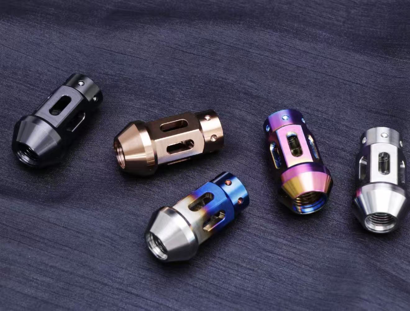 Five titanium lug nuts in different colors on a dark surface