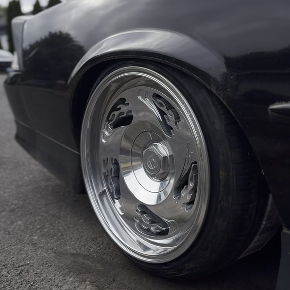 Close-up of a black car with a shiny chrome wheel with flame pattern on a road.