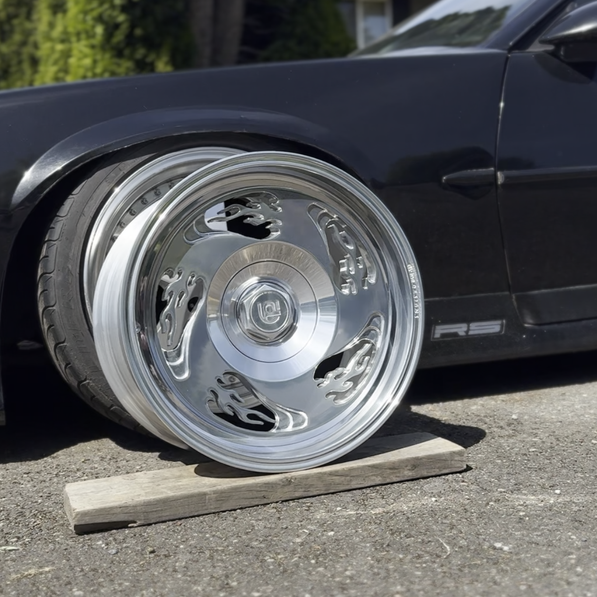 Close-up of a car wheel with a shiny flame pattern wheel on a wooden block outdoors.