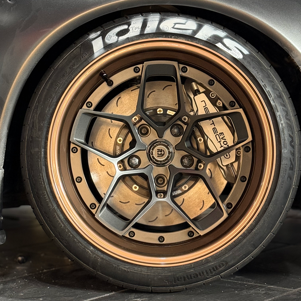 Close-up of a car wheel with a detailed rim design on a tiled floor.