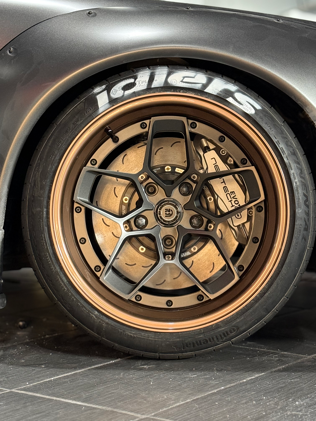 Close-up of a car wheel with a detailed rim design on a tiled floor.