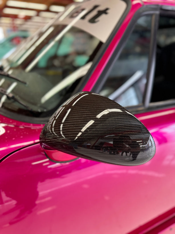 Close-up image of a one-piece seamless carbon fiber aero mirror for Porsche vehicles, displayed on a red car.