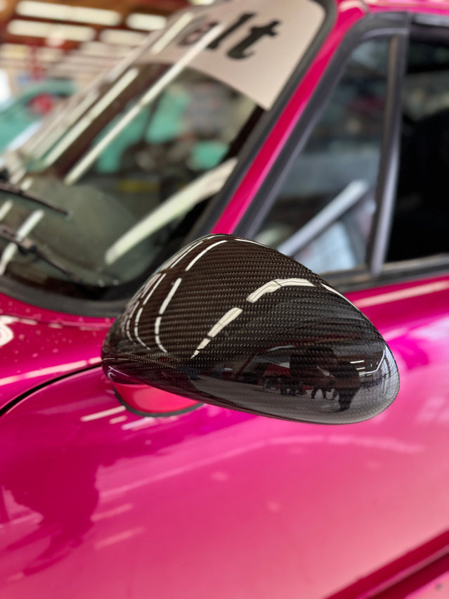 Close-up image of a one-piece seamless carbon fiber aero mirror for Porsche vehicles, displayed on a red car.
