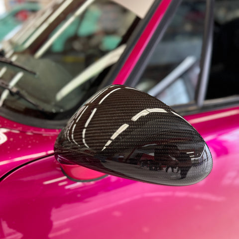Close-up image of a one-piece seamless carbon fiber aero mirror for Porsche vehicles, displayed on a red car.