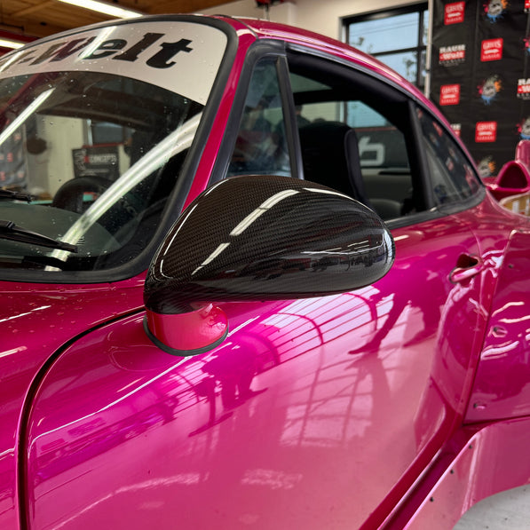 Close-up image of a one-piece seamless carbon fiber aero mirror for Porsche vehicles, displayed on a red car.