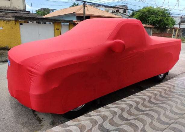 A red indoor cover with a premium embroidered logo, fitted over a vehicle parked on the side of a road.