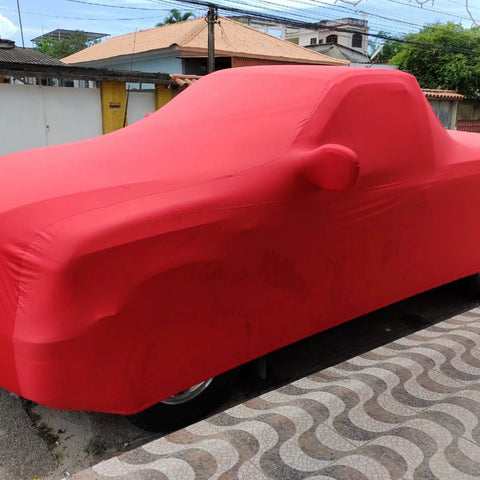 A red indoor cover with a premium embroidered logo, fitted over a vehicle parked on the side of a road.
