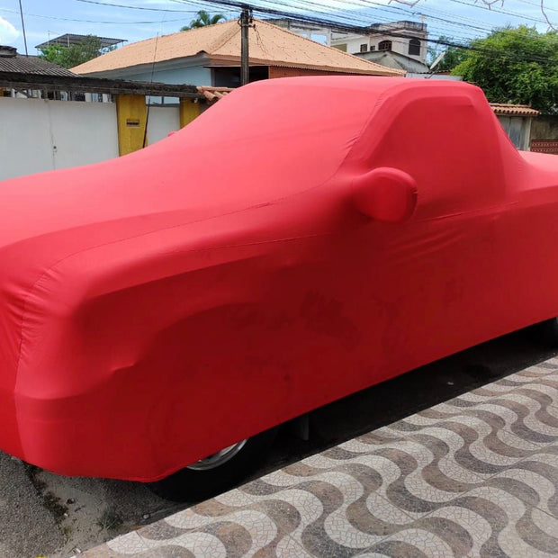 A red indoor cover with a premium embroidered logo, fitted over a vehicle parked on the side of a road.